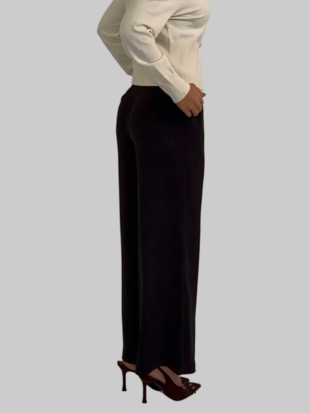 Person wearing a white sweater and black pants against a plain background