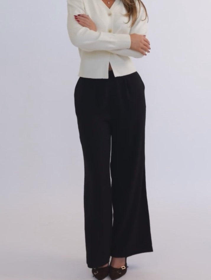 Person wearing a white sweater and black pants against a plain background